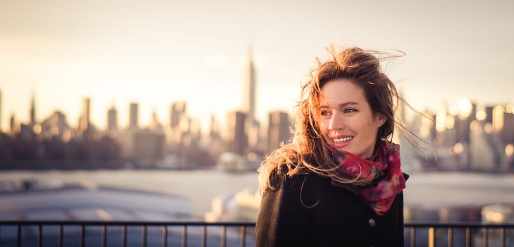Payment Gateway Services - smiling woman in coat and scarf in front of city skyline and water